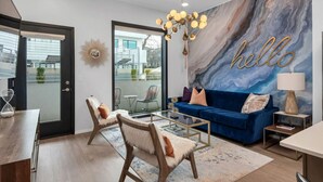 A modern living room with a blue sofa, two armchairs, a coffee table, a chandelier, and a large 'hello' wall mural.