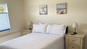 Un dormitorio con una cama grande, dos mesitas de noche con lámparas y dos cuadros colgados en la pared.