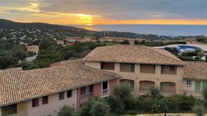 A residential area with terracotta-tiled roofs, a swimming pool, and a view of the sea at sunset. - 3bedroom flat in Les Issambres Var, superb sea view, pool and air conditioning (Roquebrune-sur-Argens)
