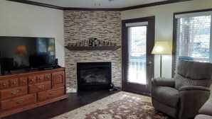 A living room with a fireplace, a television, a sofa, and a ceiling fan. - Helen Haus - RIVERFRONT 3 bdr 3.5 bath Town Home in beautiful Alpine Helen! (Helen)