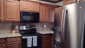 A kitchen with wooden cabinets, a stainless steel refrigerator, a microwave, and an oven. - Helen Haus - RIVERFRONT 3 bdr 3.5 bath Town Home in beautiful Alpine Helen! (Helen)