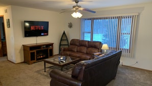 Ein Wohnzimmer mit einem braunen Ledersofa, einem Glastisch, einer Holzunterhaltungseinheit und einem an der Wand montierten Fernseher.