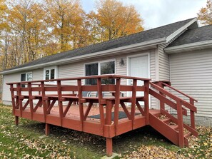 A wooden bridge leading to a white building with a dark roof, surrounded by autumn leaves.