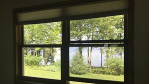 Ein Fenster mit Blick auf einen von Bäumen und Gras gesäumten See.