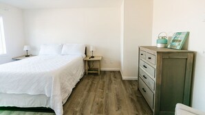 A bedroom with a bed, nightstand, dresser, and a wall-mounted shelf with a picture frame. - Cozy 2 Bedroom with Full Kitchen One Block from the Ocean!! (Crescent City)