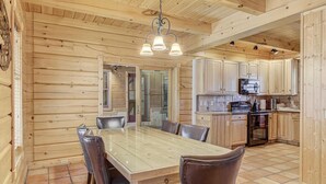 A wooden interior with a dining table, chairs, a kitchen area, and a ceiling light fixture. - Gorgeous Cabin w/direct trail access for hiking & off roading! (Payson)