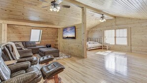 A spacious room with wooden walls and floors, a large window, a ceiling fan, and a sofa with leather chairs. - Gorgeous Cabin w/direct trail access for hiking & off roading! (Payson)