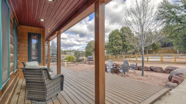 A wooden deck with wicker furniture and a view of a landscaped area with trees and rocks. - Gorgeous Cabin w/direct trail access for hiking & off roading! (Payson)
