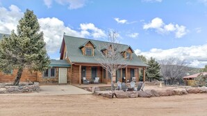 A two-story log cabin with a green roof, a covered patio with outdoor seating, and a stone retaining wall. - Gorgeous Cabin w/direct trail access for hiking & off roading! (Payson)