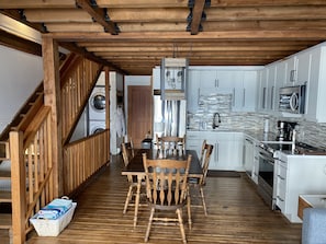 Cozy cabin kitchen with dining area, featuring a wooden dining table, stove, and sink area, plus modern appliances and laundry facilities.