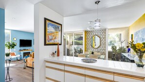 Een moderne keuken met een groot schiereiland, een eethoek met een tafel en stoelen, een televisie en een ingelijste foto aan de muur.