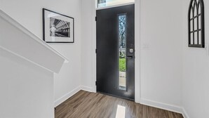 Ein Flur mit einer schwarzen Tür, einem gerahmten Bild an der Wand und einem Fenster mit Blick auf Grünfläche.