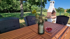 An outdoor dining area with a wooden table, chairs, a vase with dried flowers, and a bowl of cherries. - Comfortable single family home on the east coast of Istria peninsula (Štrmac)