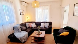 A living room with a dark patterned sofa, a wooden coffee table with a vase, a green armchair, and a black ottoman. - Comfortable single family home on the east coast of Istria peninsula (Štrmac)
