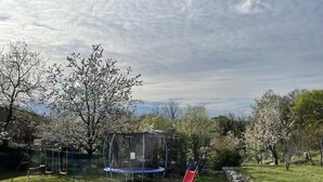 A grassy outdoor area with a trampoline, a red slide, and trees. - Comfortable single family home on the east coast of Istria peninsula (Štrmac)