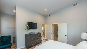 A bedroom with a bed, a dresser, a TV, and a door leading to another room. - Funky Modern Home Minutes Drive from Downtown CLE (Cleveland)