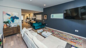 A modern living room with a sofa, a teal armchair, and a coffee table. There is a kitchen in the background with a dining area. - Funky Modern Home Minutes Drive from Downtown CLE (Cleveland)