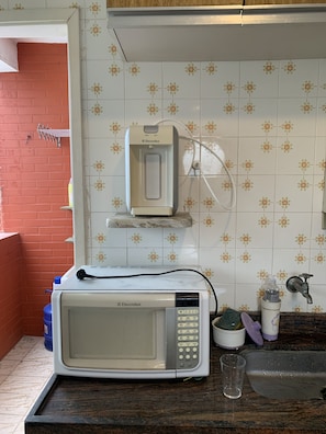 Kitchen area with microwave, water dispenser, and storage container.