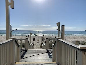 Une vue sur la plage depuis un escalier en bois menant à une plage de sable où se trouvent des personnes et des parasols.