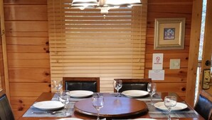 Een houten eetkamer met een ronde tafel voor vier personen, met donkere stoelen met een kruiselings rugontwerp.