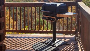 Een houten terras met een barbecue, een bakstenen muur en uitzicht op herfstkleurige bomen en bergen.