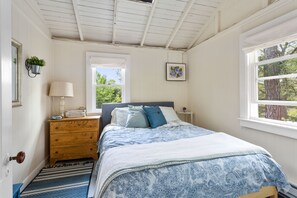 A bedroom with a bed, dresser, lamp, and windows. - Historic Cottage on White Pond, near Downtown Chatham and beaches (Chatham)