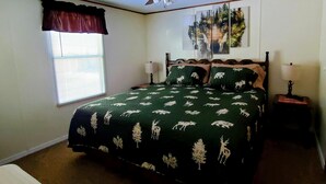 A bedroom with a bed, two bedside tables, a window with blinds, a ceiling fan, and a wall-mounted painting. - Iron Wolf nestled in the Sangre de Cristo Mtns...Ski/Hike/Fish/Hunt Casita (Eagle Nest)