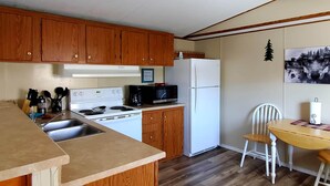 A kitchen with wooden cabinets, a stove, a microwave, a refrigerator, and a dining table with chairs. - Iron Wolf nestled in the Sangre de Cristo Mtns...Ski/Hike/Fish/Hunt Casita (Eagle Nest)