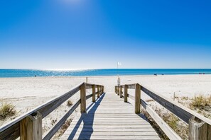 A wooden boardwalk leading to a beach with a flag in the distance.