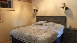 A bedroom with a wooden bed, a dark headboard, two bedside tables with lamps, and a wooden floor. - Log Home on the Blackfoot River (Lincoln)