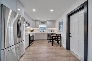 A modern kitchen with stainless steel appliances, a dining area with wooden chairs, and a white door.