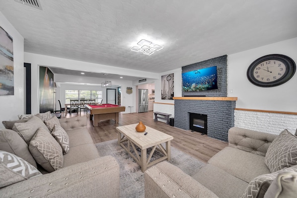 A spacious living room with a pool table, comfortable sofas, a fireplace, and a large TV.