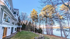 A two-story house with a stone retaining wall and a grassy yard. - Oceanfront, views from every room! Sunny, spacious midcoast retreat (Round Pond)