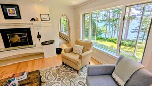 A living room with a fireplace, a sofa, a chair, and a view of a lake. - Oceanfront, views from every room! Sunny, spacious midcoast retreat (Round Pond)