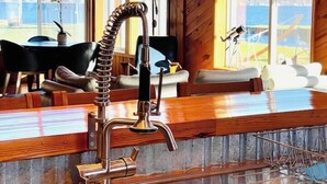 Uma cozinha com armários de madeira, uma pia de aço inoxidável e vista para o exterior através de grandes janelas.
