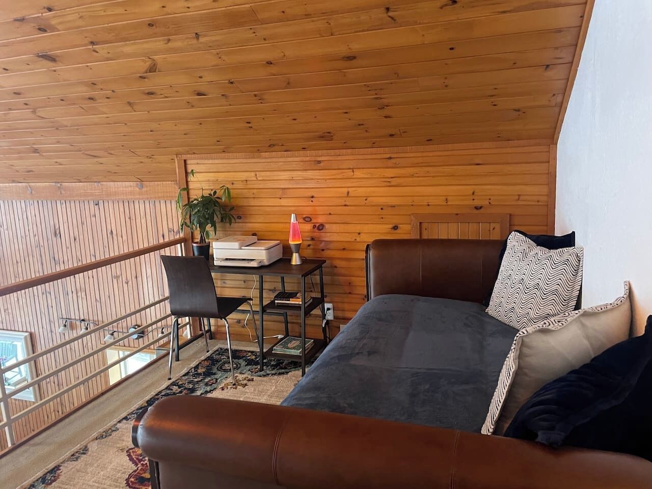 Een gezellige kamer met houten plafond, een bed met kussens, een bureau met lamp en uitzicht door een balkonhek.