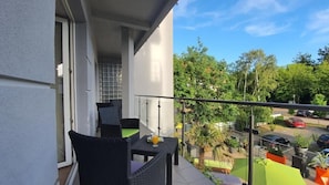 A balcony with wicker furniture, a glass door, and a view of a parking area and trees. - Villa Delfin SPA (Swinoujscie)