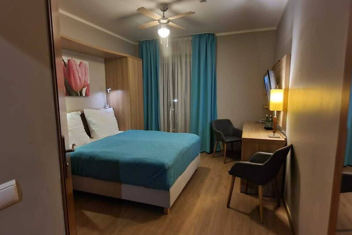 Ein Hotelzimmer mit einem Bett, einem Schreibtisch, zwei Stühlen, einem Deckenventilator und einem Fernseher.