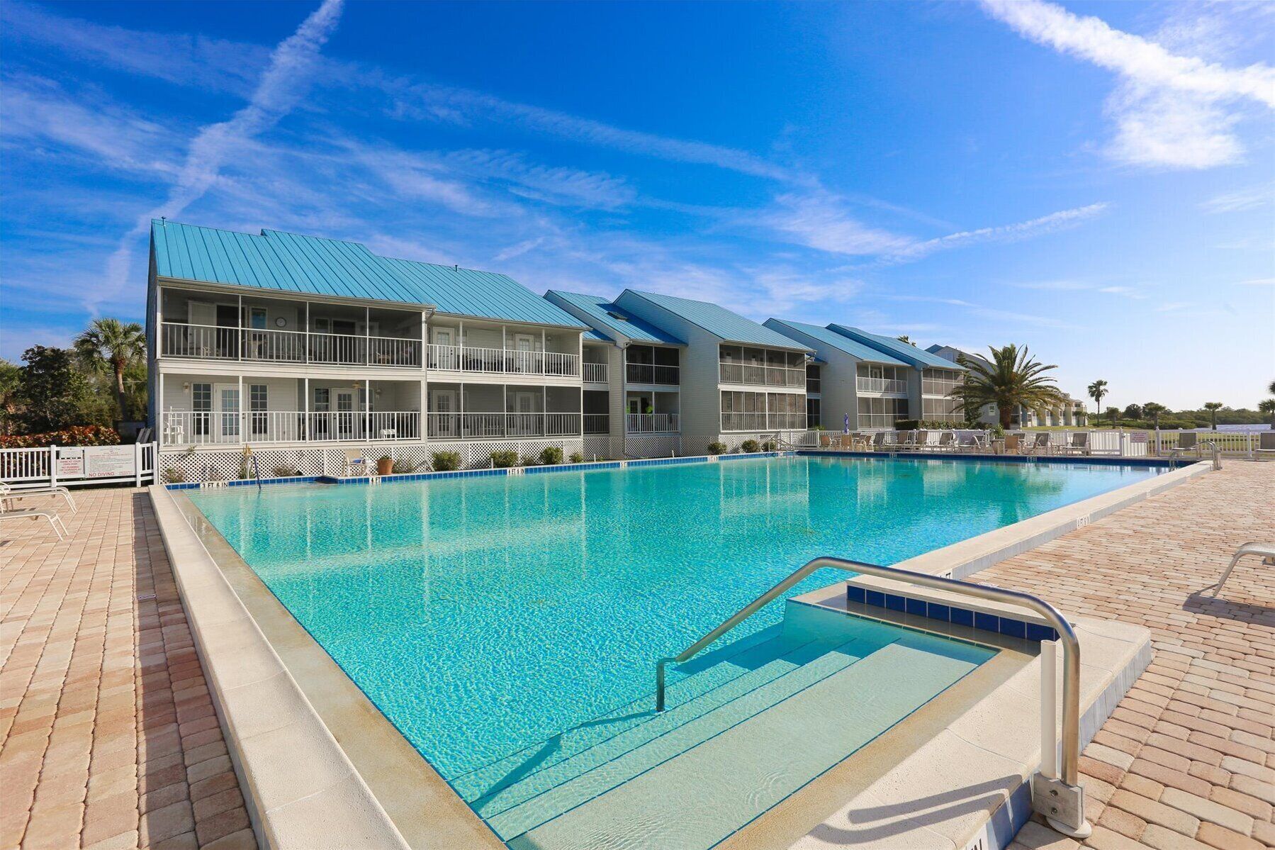 A hotel with a large pool, multiple balconies, and a clear blue sky.