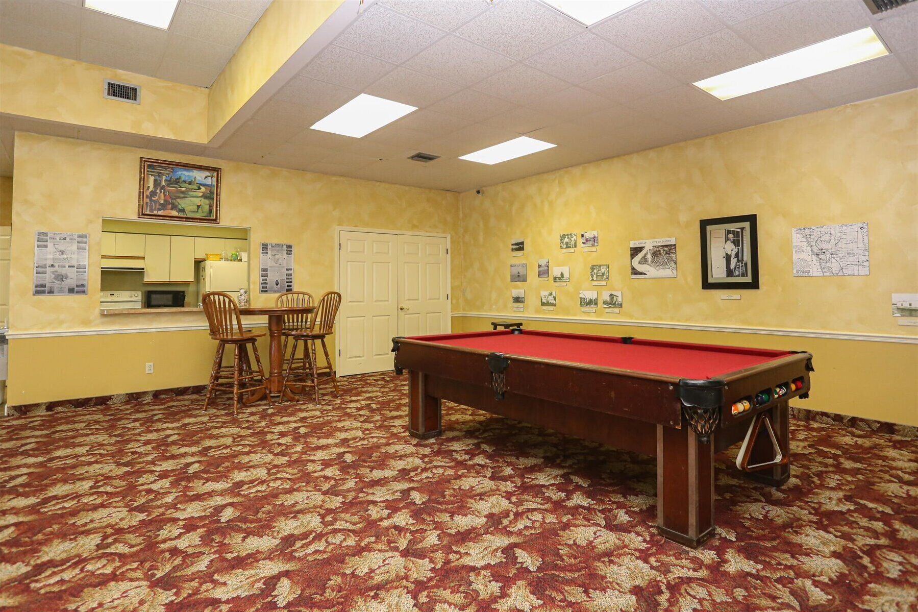 A room with a pool table, chairs, a small kitchen area, and a door.
