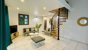 Ein geräumiger Wohnbereich mit moderner Treppe, einem Flachbildfernseher und einer großen Pflanze.