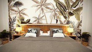 Ein Schlafzimmer mit Bett, Holz-Kopfstück, zwei Nachttischen, zwei Lampen und einem Wandbild mit tropischem Motiv.