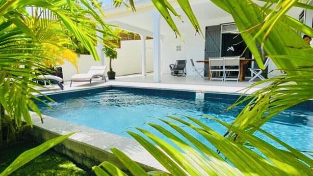 Ein Pool, umgeben von üppigem Grün, mit Liegestühlen und einer überdachten Sitzgelegenheit.