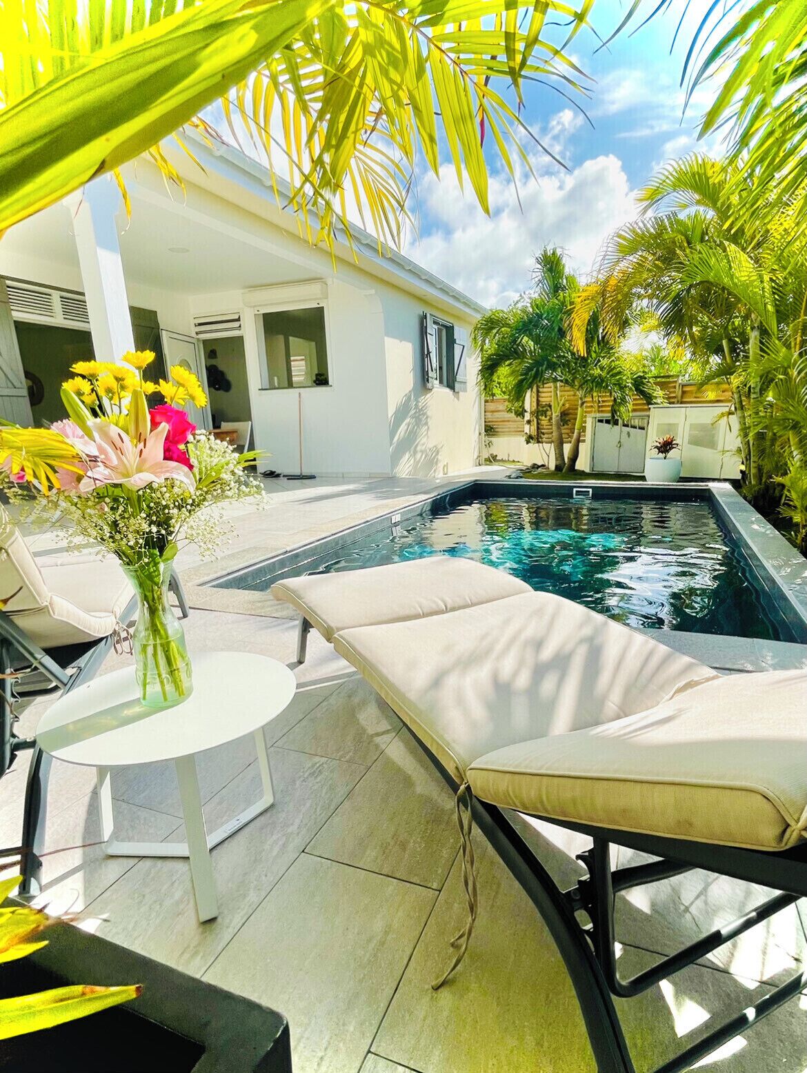 A poolside area with lounge chairs, a small table, and a flower arrangement.