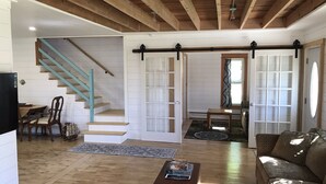 A spacious living area with a wooden staircase, a sliding door, a sofa, and a coffee table. - Charming Historic Mackinaw City Cottage (Mackinaw City)
