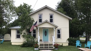 A two-story house with a front porch, a welcome sign, and an American flag. - Charming Historic Mackinaw City Cottage (Mackinaw City)