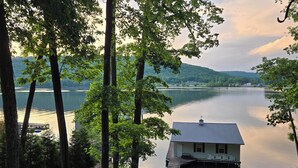 A lakeside cabin with a dock, surrounded by tall trees and a view of the lake and distant hills. - Honeycomb Waterfront Lakehouse with deep water dock (Grant)