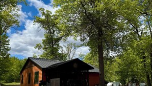 Eine rustikale Holzhütte mit Veranda, umgeben von Bäumen und blauem Himmel.