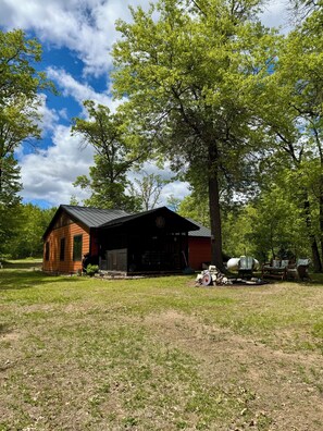 A rustic cabin with a porch, surrounded by trees and a clear sky.