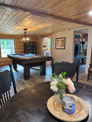 A wooden dining area with a pool table, chairs, and a vase with flowers.